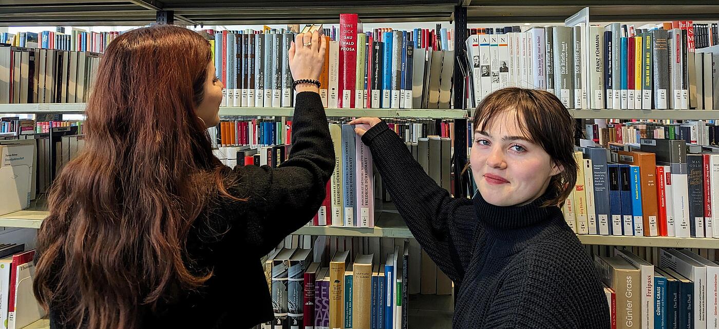 Foto von den beiden Freiwilligen Irem und Milena am Bücherregal