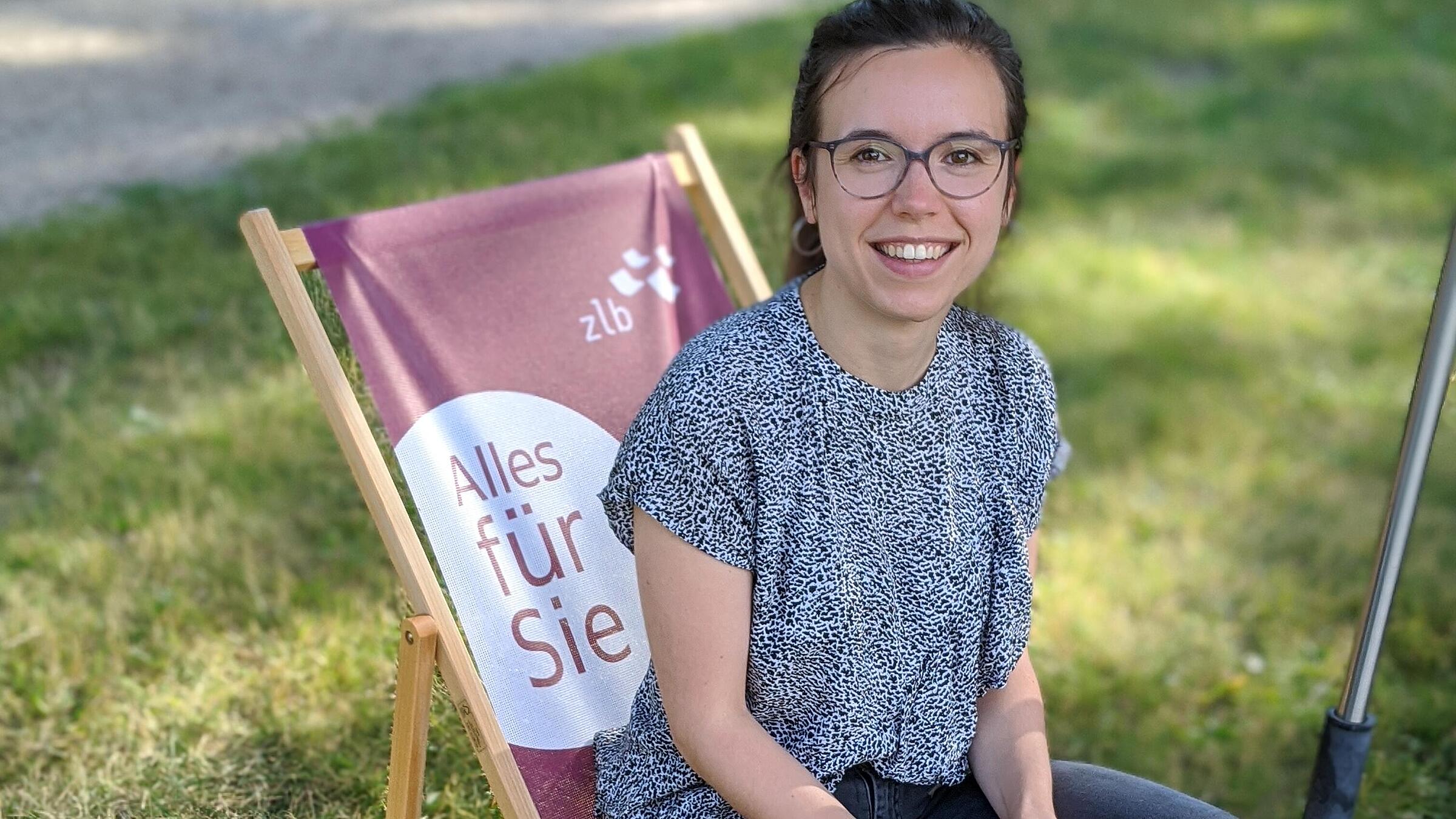 Young woman sitting on deck chair in fresh air library smiling at camera