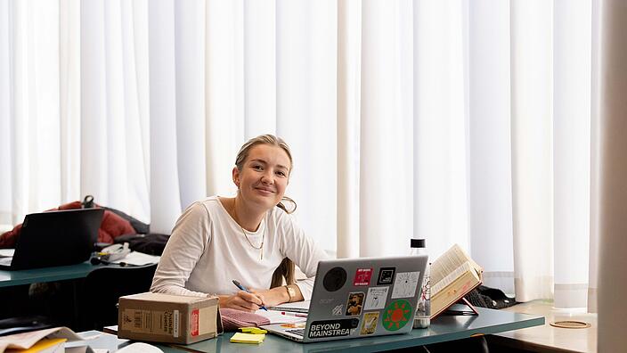 Frau sitzt fröhlich an Laptop in Bibliothek