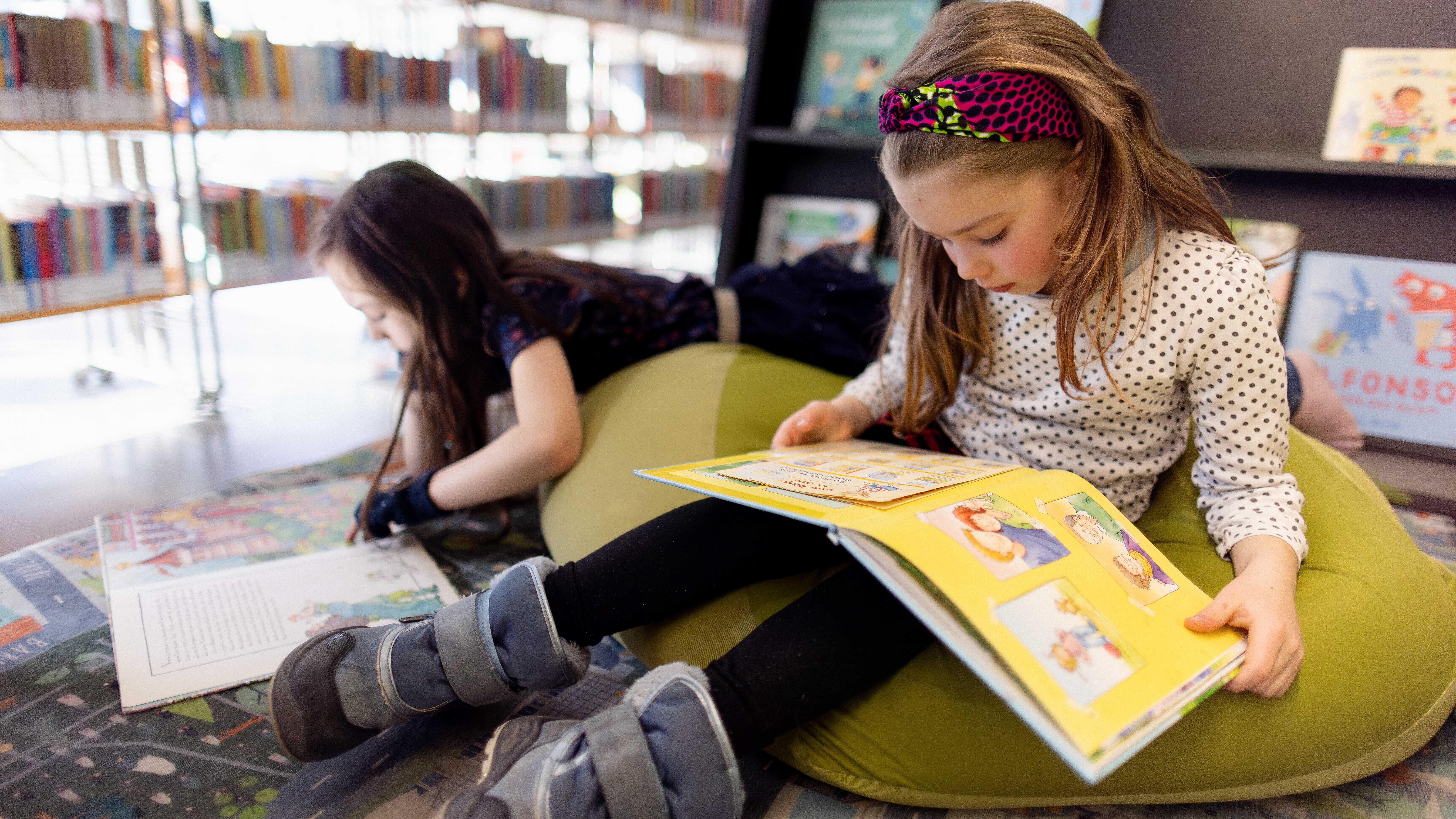 Foto von zwei Kindern in der KiJuBi der ZLB, die auf Sitzkissen ein Buch lesen