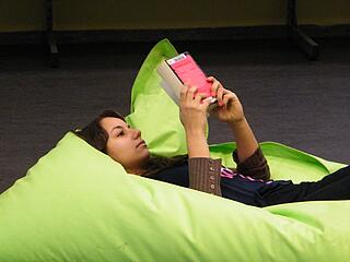 Jugendliche liegt auf grünem Sitzsack in der KiJuBi und schmökert in einem Buch