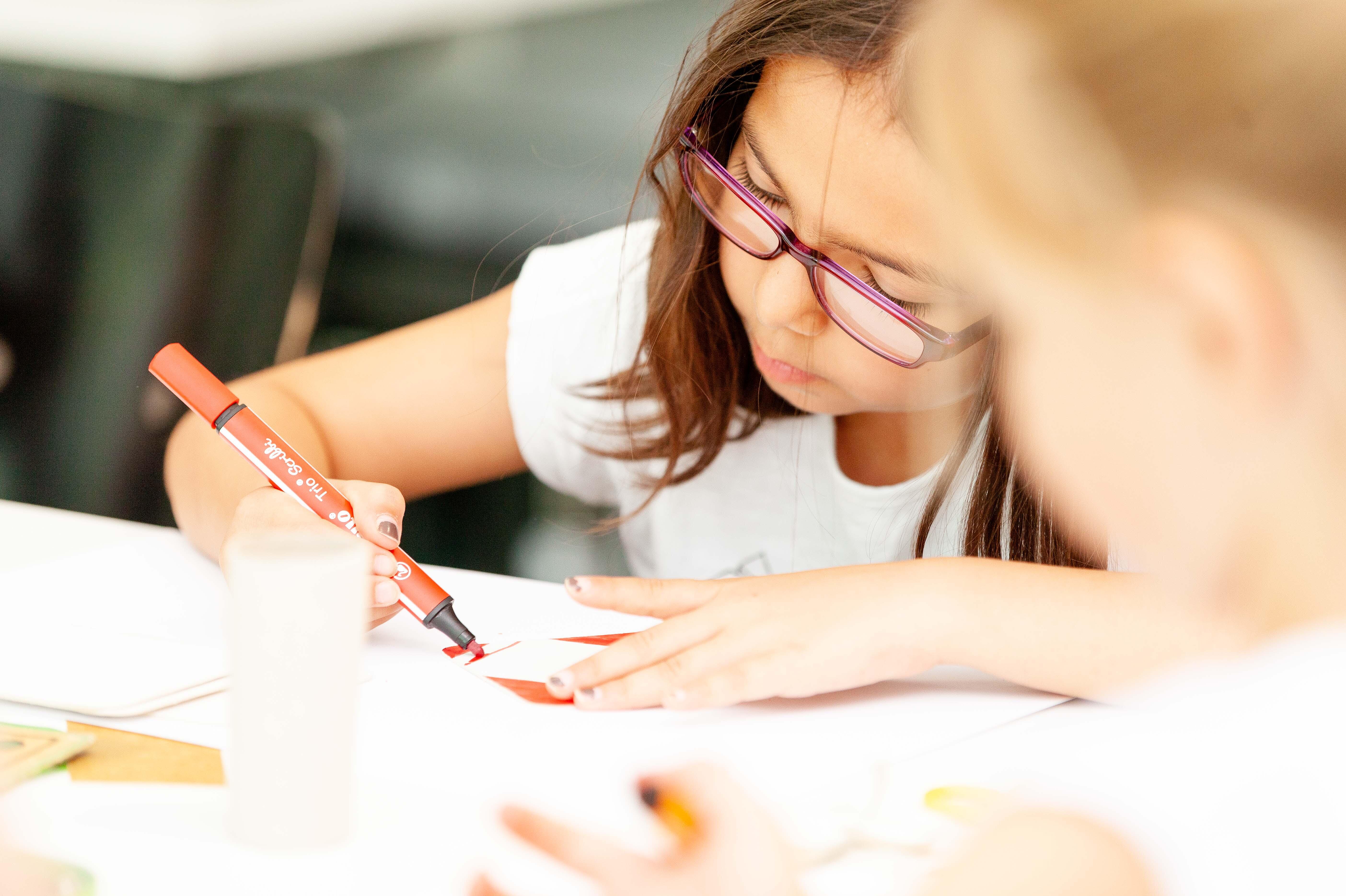 Mädchen, das konzentriert mit einem Filzstift auf weißem Papier malt