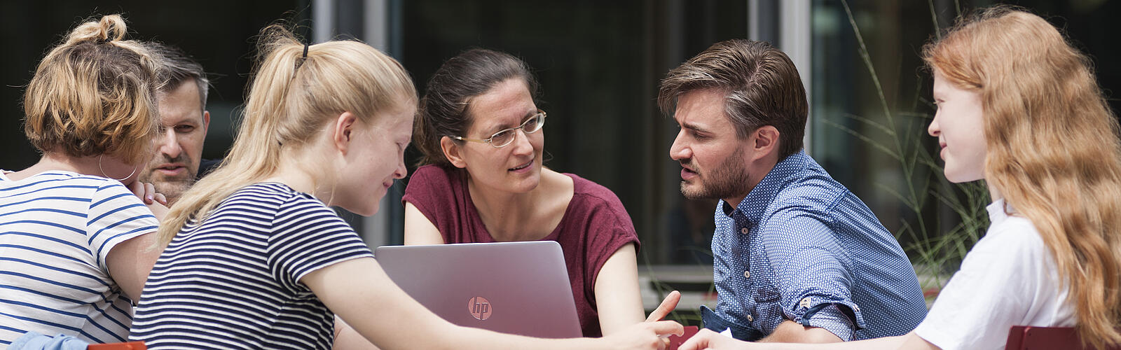 People sit together in the courtyard at a table with a laptop and talk to each other