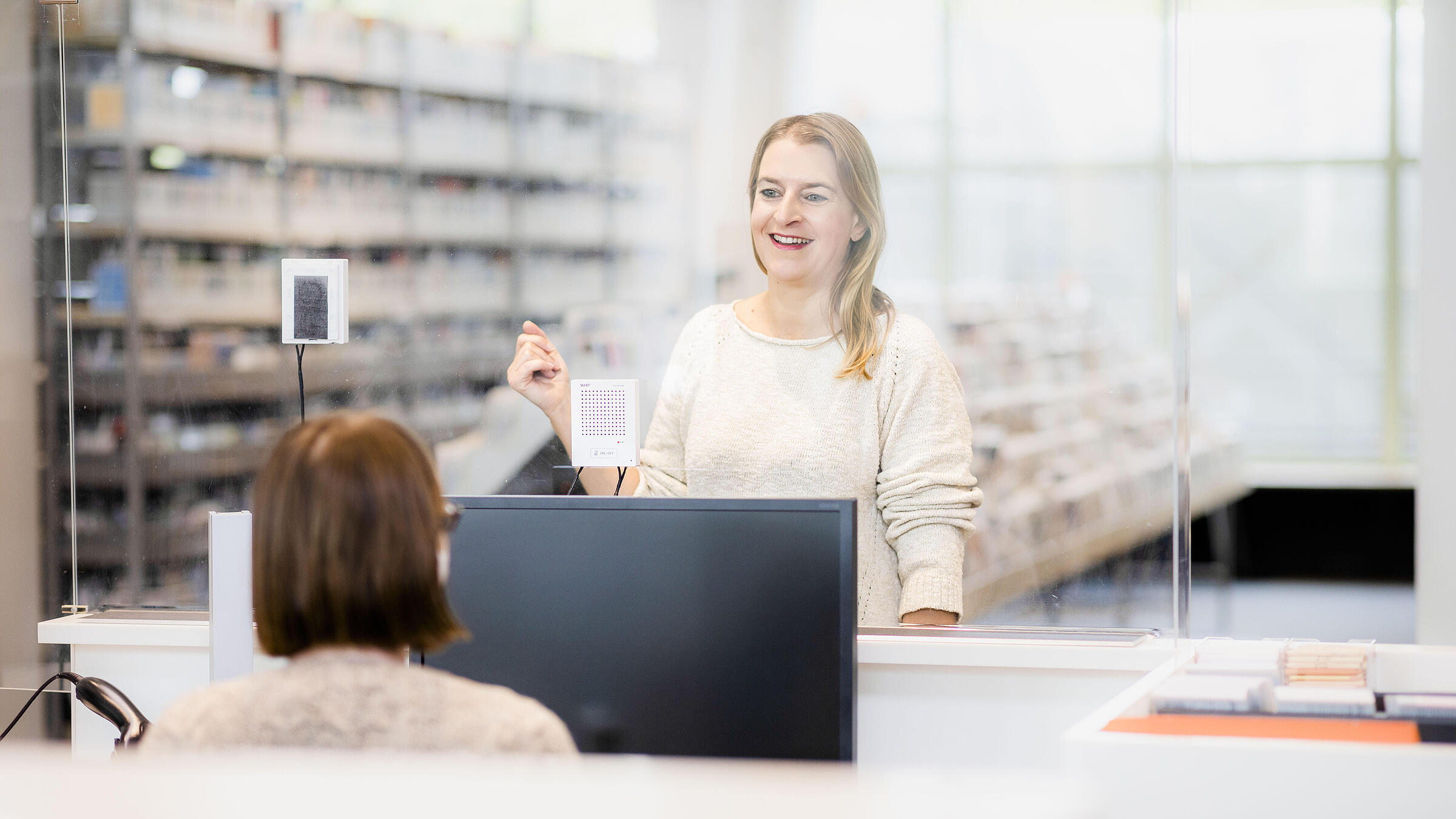 Frau steht an der Infotheke und ist im Austausch mit der Bibliothekarin