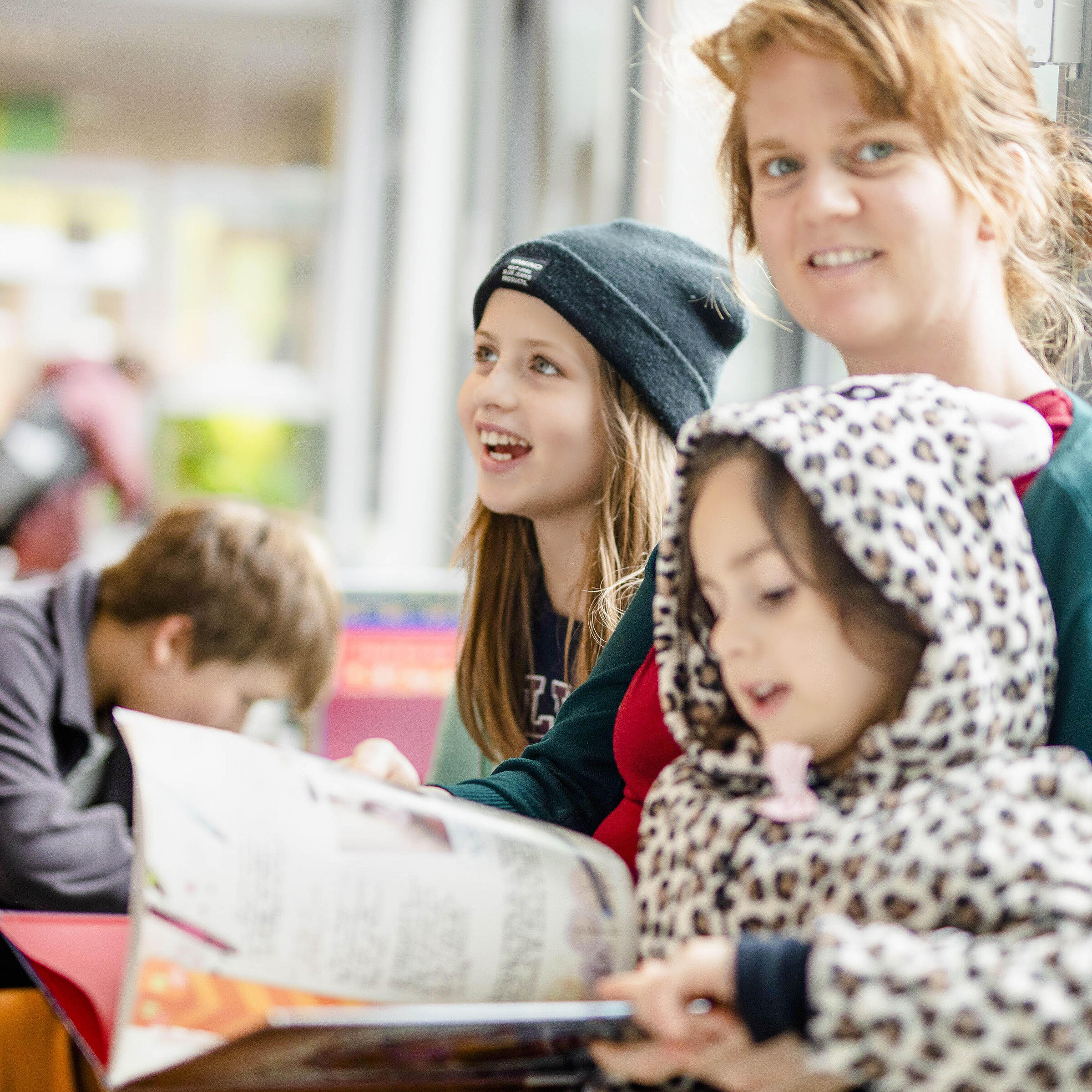 Mutter mit drei Kindern und Buch auf dem Schoß in der Kinder- und Jugendbibliothek