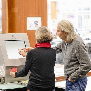 Zwei Menschen zeigen auf Bildschirm des technischen Gerätes zur Selbstverbuchung in Bibliothek