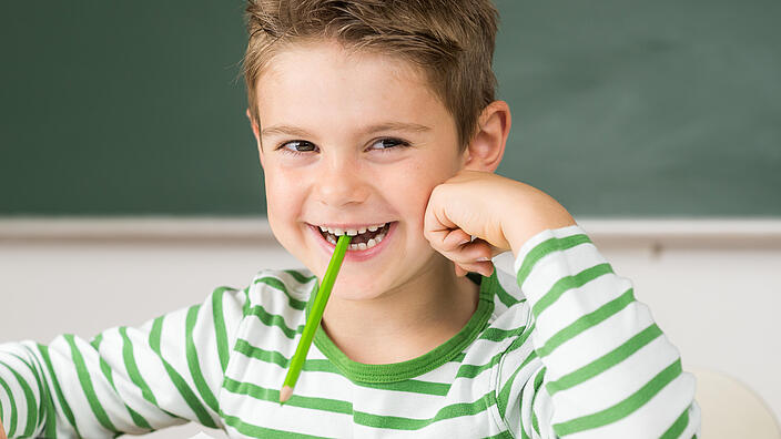 Junge mit Bleistift im Mund lächelt in Kamera