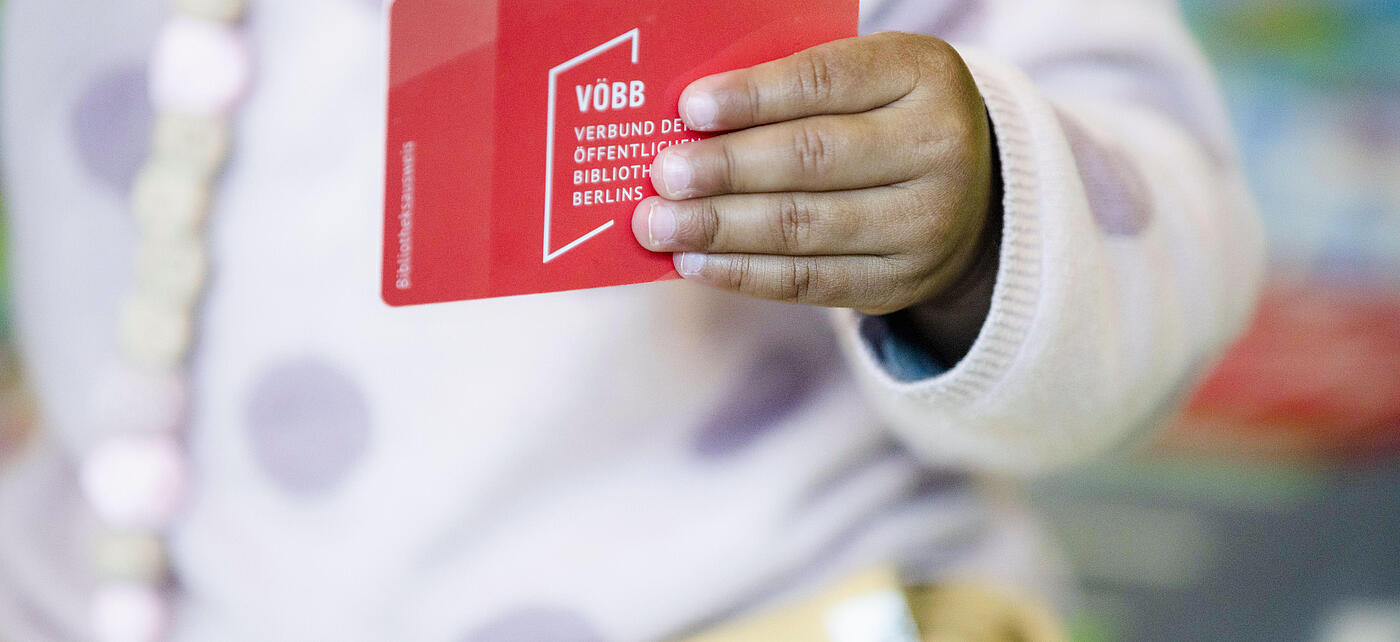 Baby hält Bibliotheksausweis mit Aufschrift "VÖBB Verbund der öffentlichen Bibliotheken Berlins"