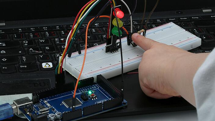 Coding Arduino, Foto einer Tastatur und eines Fingers, der ein technisches Gerät bedient.