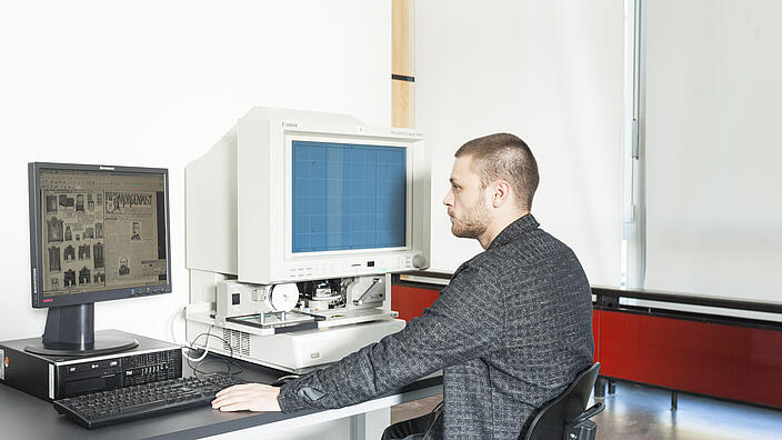 Junger Mann sitzt an Mikrofilmlesegerät