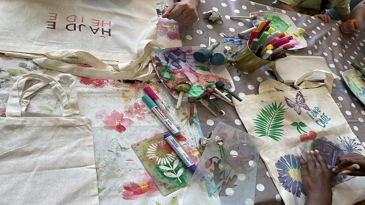 Basteltisch aus der Vogelperspektive mit Beuteln die gerade bedruckt werden mittels bunter Stifte, Schwämmen mit Farbe und Schablonen 