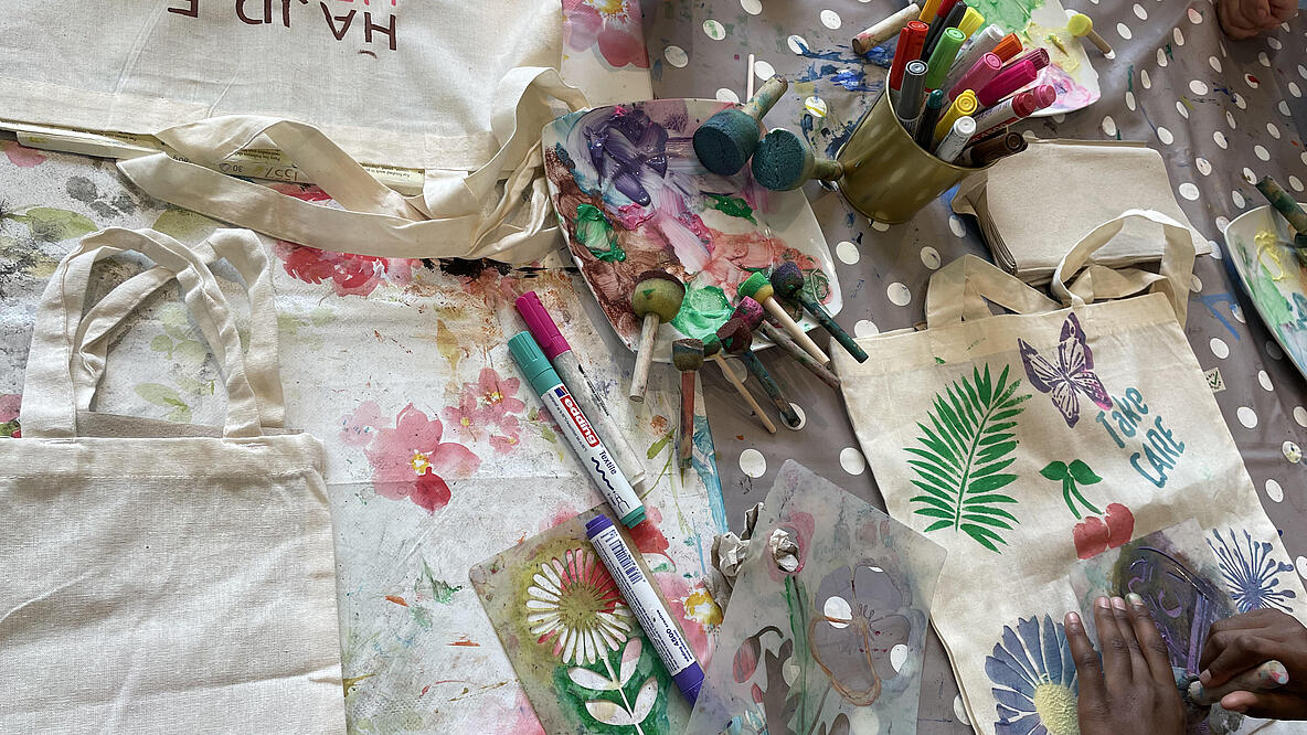 Basteltisch aus der Vogelperspektive mit Beuteln die gerade bedruckt werden mittels bunter Stifte, Schwämmen mit Farbe und Schablonen 