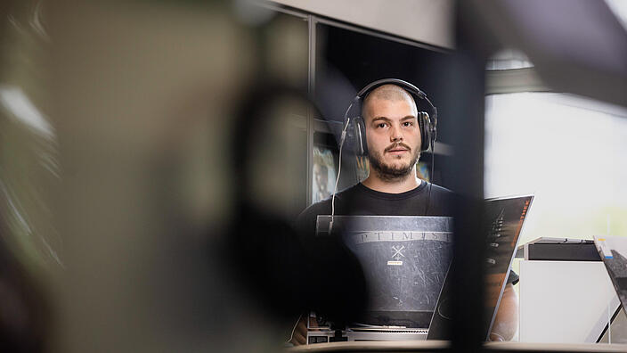 Junger Mann mit Kopfhörern steht an Schallplattenspieler in der Phonothek im Salon der AGB