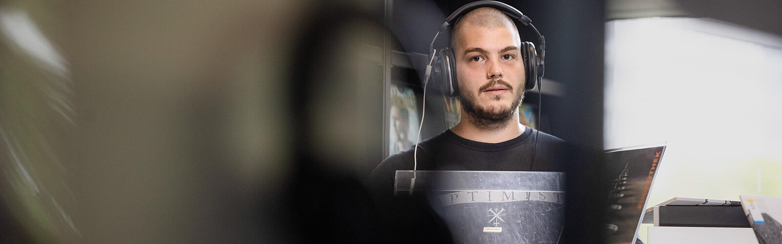 Junger Mann mit Kopfhörern steht an Schallplattenspieler in der Phonothek im Salon der AGB
