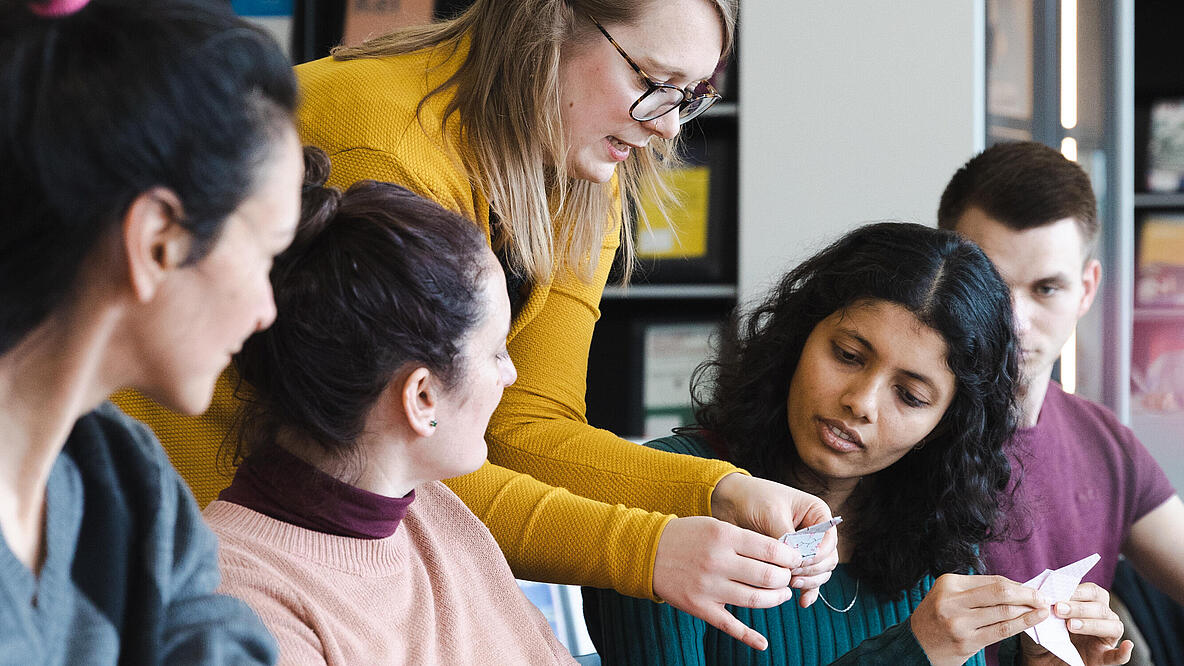 4 Frauen und eine Mann arbeiten gemeinsam im Salon der AGB an einem Tisch und falten Origami