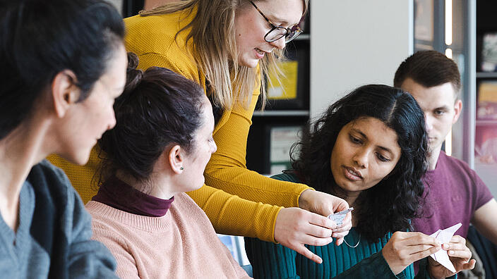 4 Frauen und eine Mann arbeiten gemeinsam im Salon der AGB an einem Tisch und falten Origami