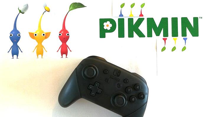 Foto eines Controllers und Darstellung von drei bunten Figuren und dem Schriftzug "Pikmin"