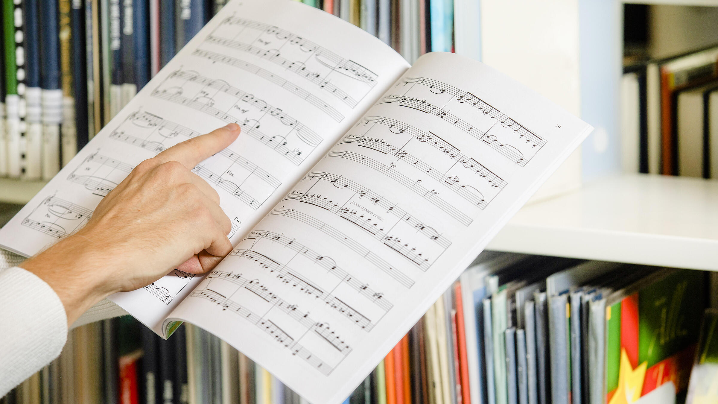 Finger zeigt auf gedruckte Noten in aufgeschlagenem DIN A4-Buch in Bibliothek