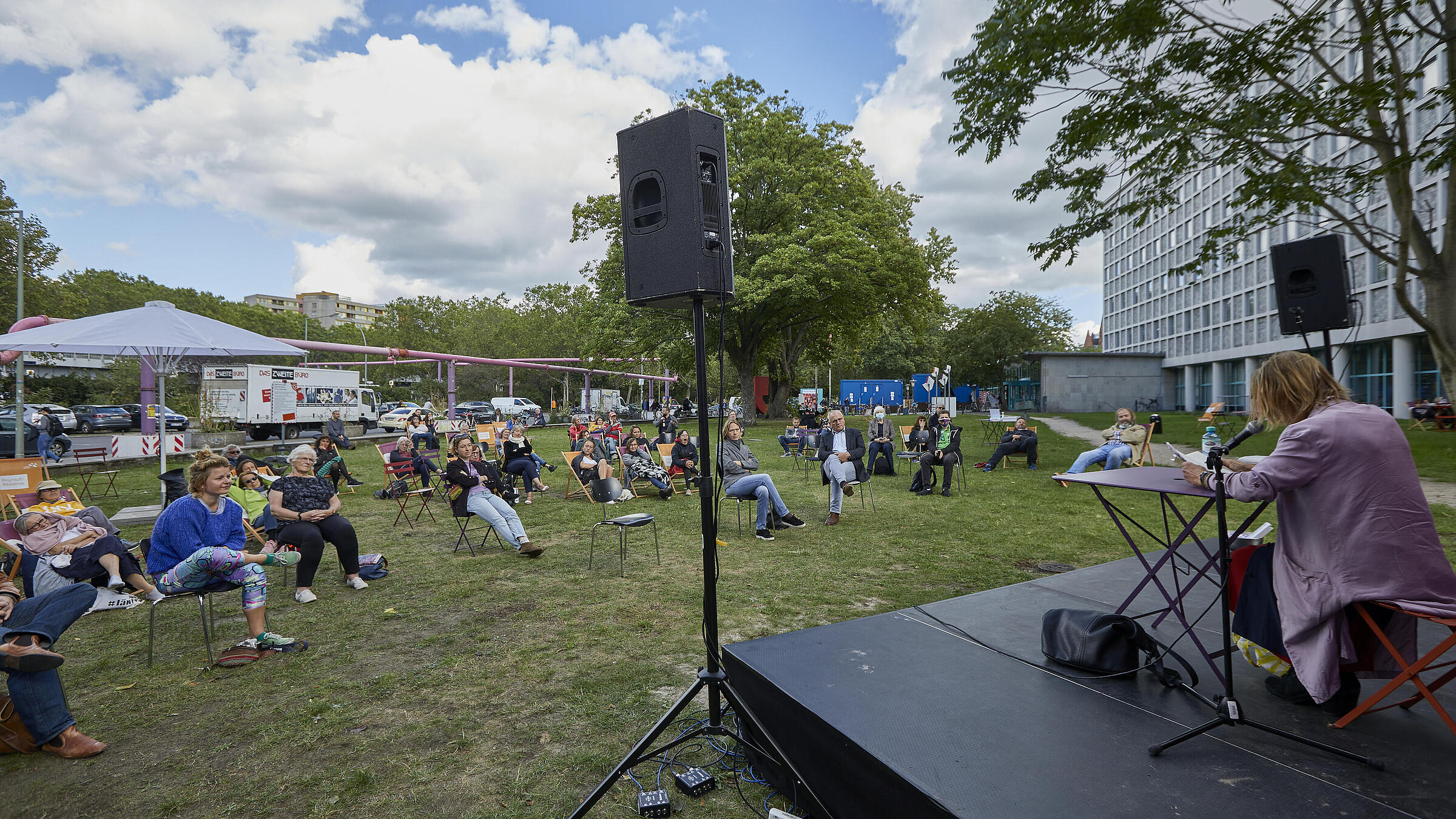 Event on the meadow of the AGB with audience in deck chairs, a stage and an author reading aloud