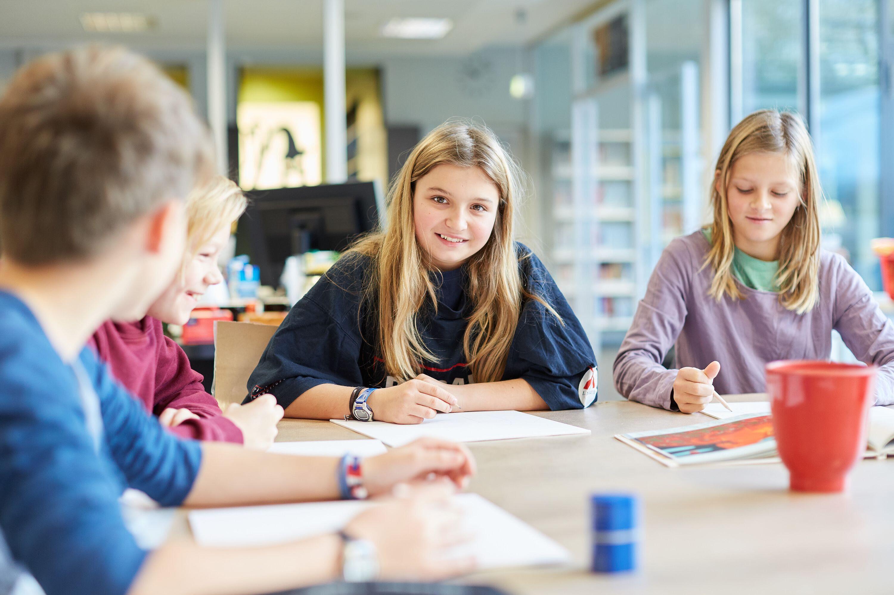 Kinder, die fröhlich mit Heften und Stiften an Tisch in Bibliothek sitzen