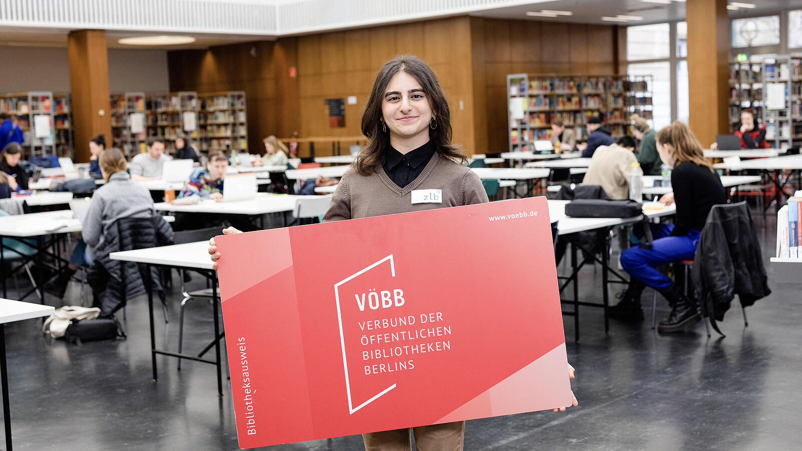 Junge Frau mit sehr großem Bibliotheksausweis in der Lesehalle der BStB