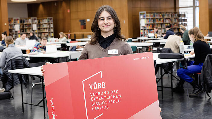 Junge Frau mit sehr großem Bibliotheksausweis in der Lesehalle der BStB
