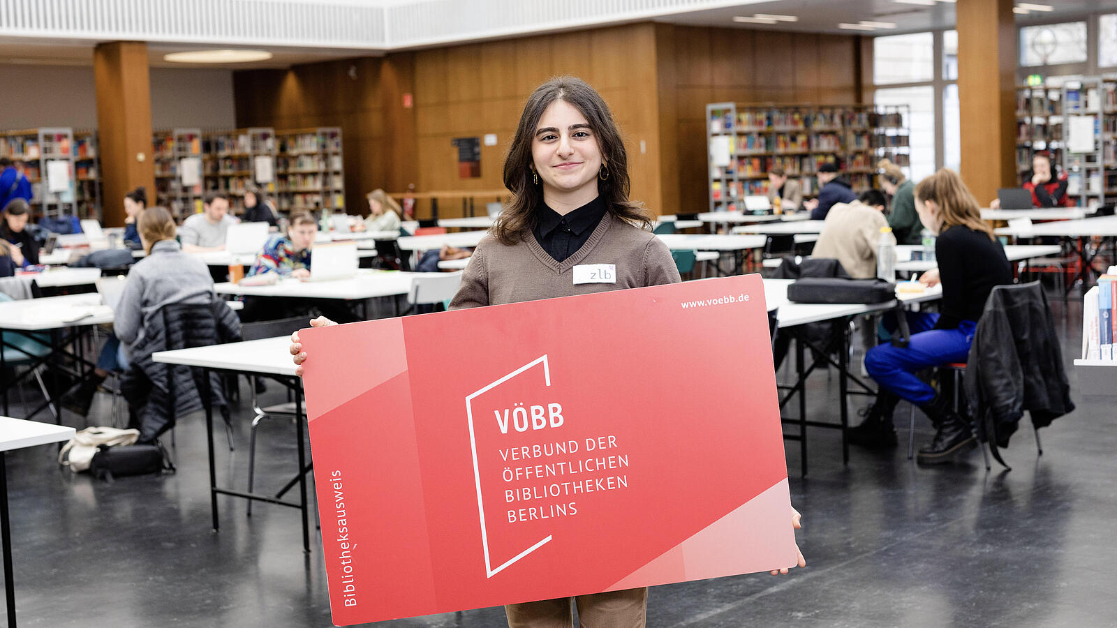 Junge Frau mit sehr großem Bibliotheksausweis in der Lesehalle der BStB