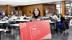 Junge Frau mit sehr großem Bibliotheksausweis in der Lesehalle der BStB