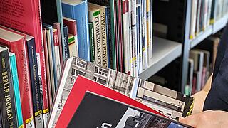 Hände halten augeschlagenes Buch mit dem Titel "Stadt Mitte Berlin" vor Regal