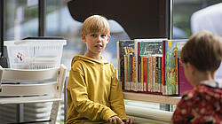 Junge sitzt an Spielebox vor Büchern in der KiJuBi