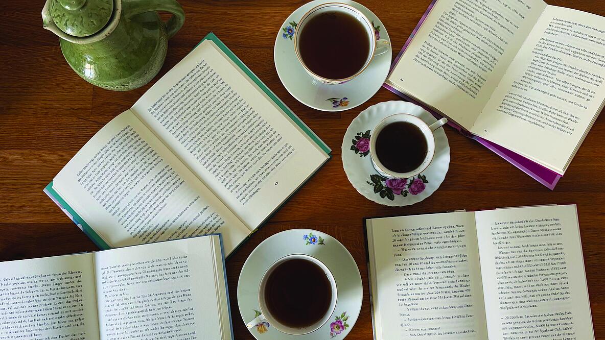 Foto von vier aufgeschlagenen Büchern und drei Tassen Tee auf einem Tisch