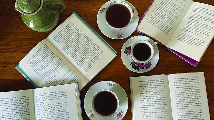 Foto von vier aufgeschlagenen Büchern und drei Tassen Tee auf einem Tisch