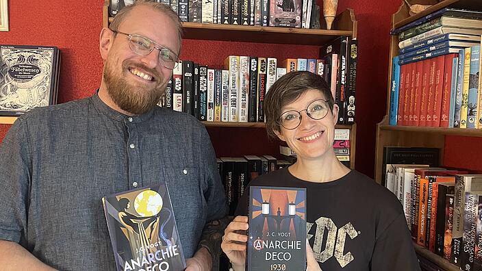 Porträt von Judith und Christian Vogt vor einer bunten Bücherwand