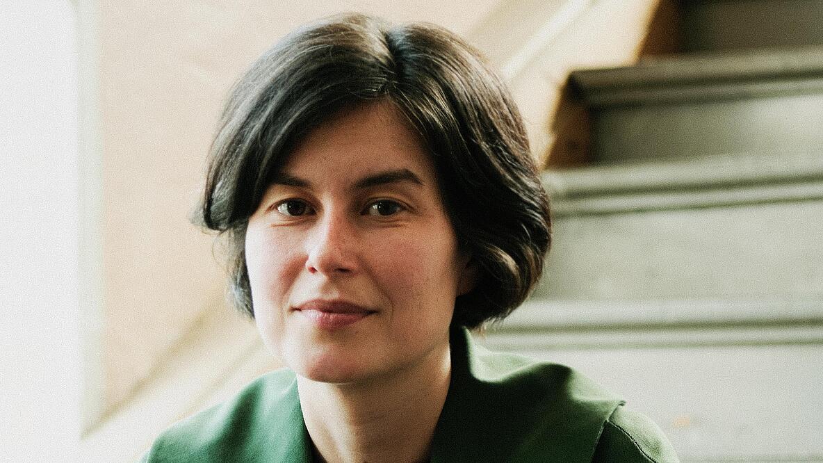 Foto des Oberkörpers einer Person, die auf einer Treppe sitzend in die Kamera schaut.