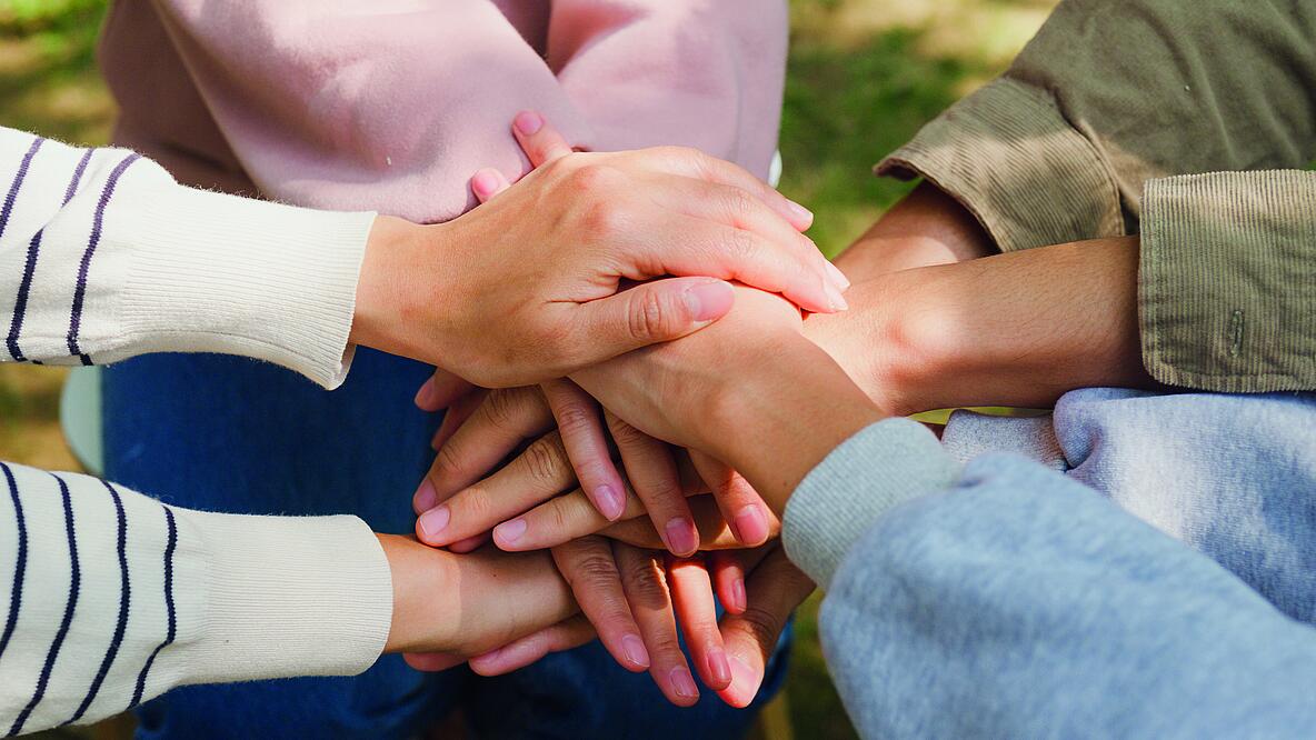 Foto von im Wechsel übereinandergelegten Händen von vier Personen