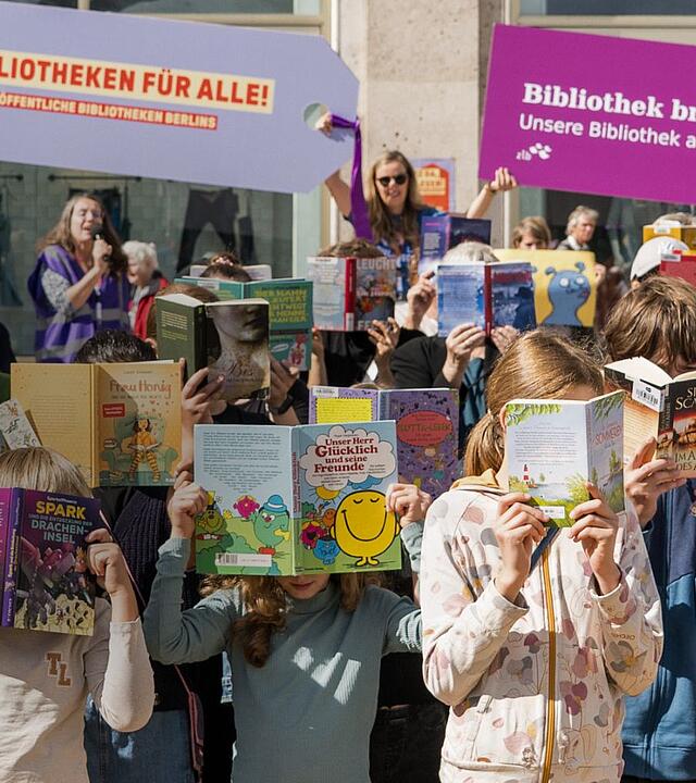 Kinder halten Bücher vor Ihre Gesichter auf dem Alexanderplatz