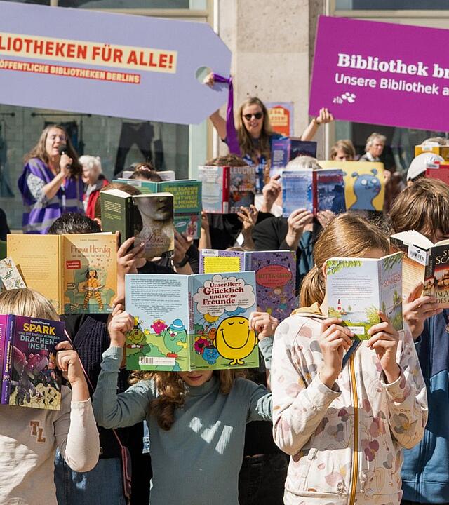 Kinder halten Bücher vor Ihre Gesichter auf dem Alexanderplatz