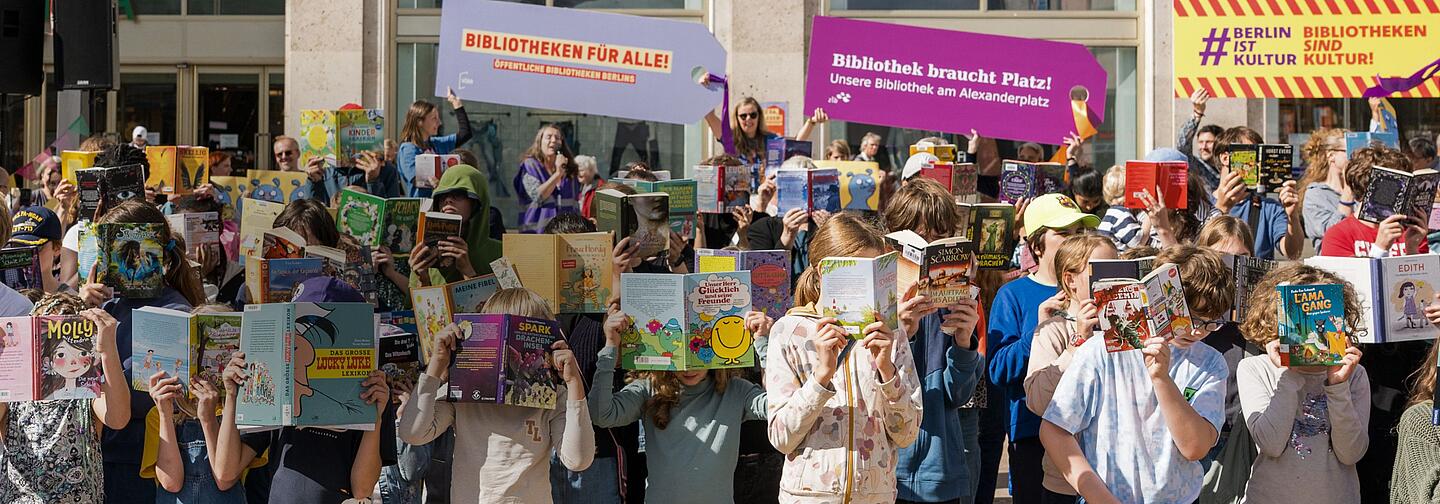 Kinder halten Bücher vor Ihre Gesichter auf dem Alexanderplatz