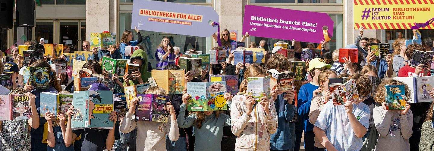 Kinder halten Bücher vor Ihre Gesichter auf dem Alexanderplatz