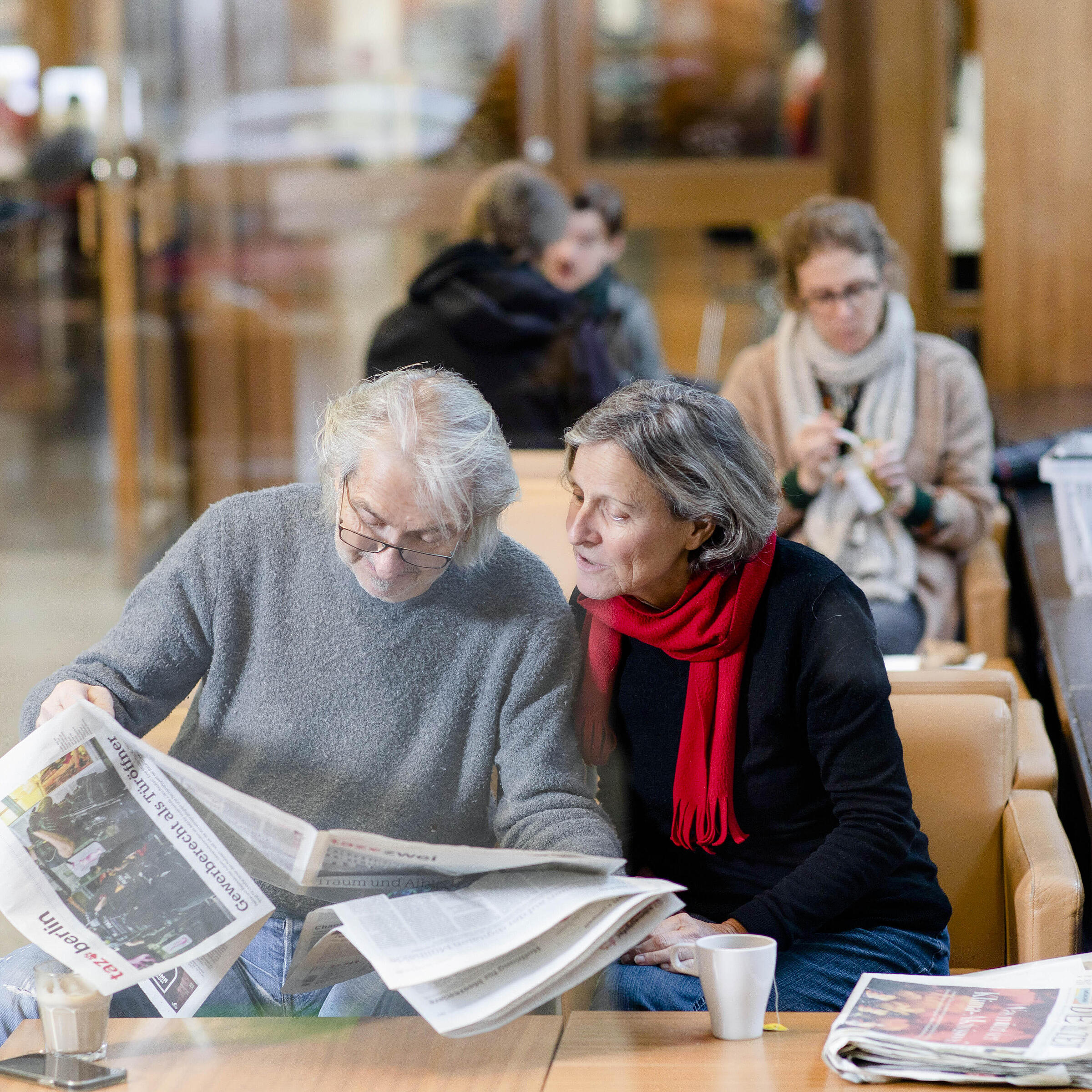 Menschen sitzen mit Heißgetränken und Zeitung im Café der Berliner Stadtbibliothek
