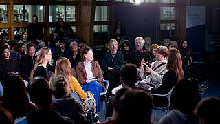 In einer Fish Bowl sitzen fünf Personen und diskutieren rege miteinander. Im Hintergrund sitzt das Publikum im Kreis um die Diskutant*innen.