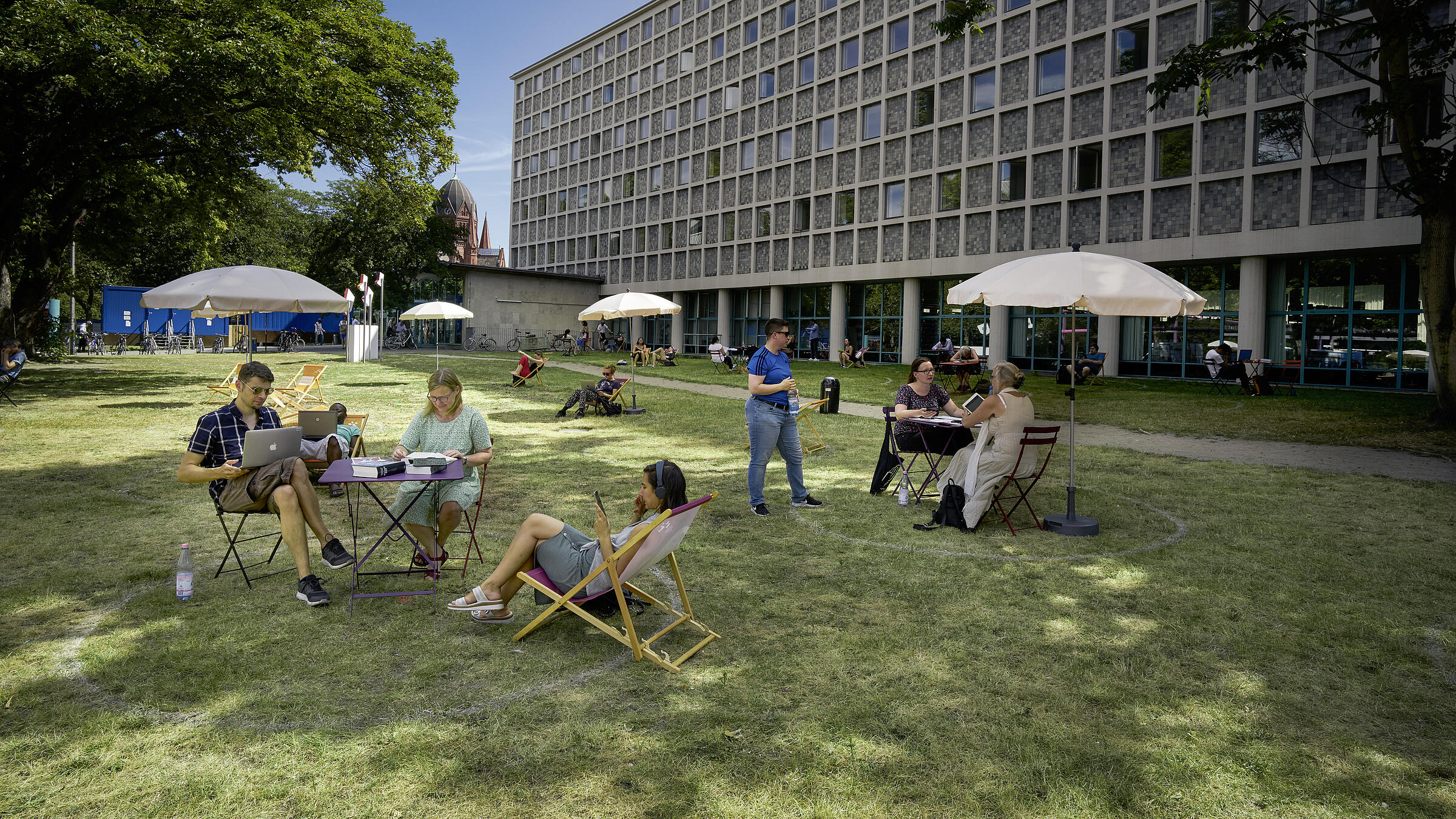 People sitting on tables and deck chairs on the lawn in front of the AGB