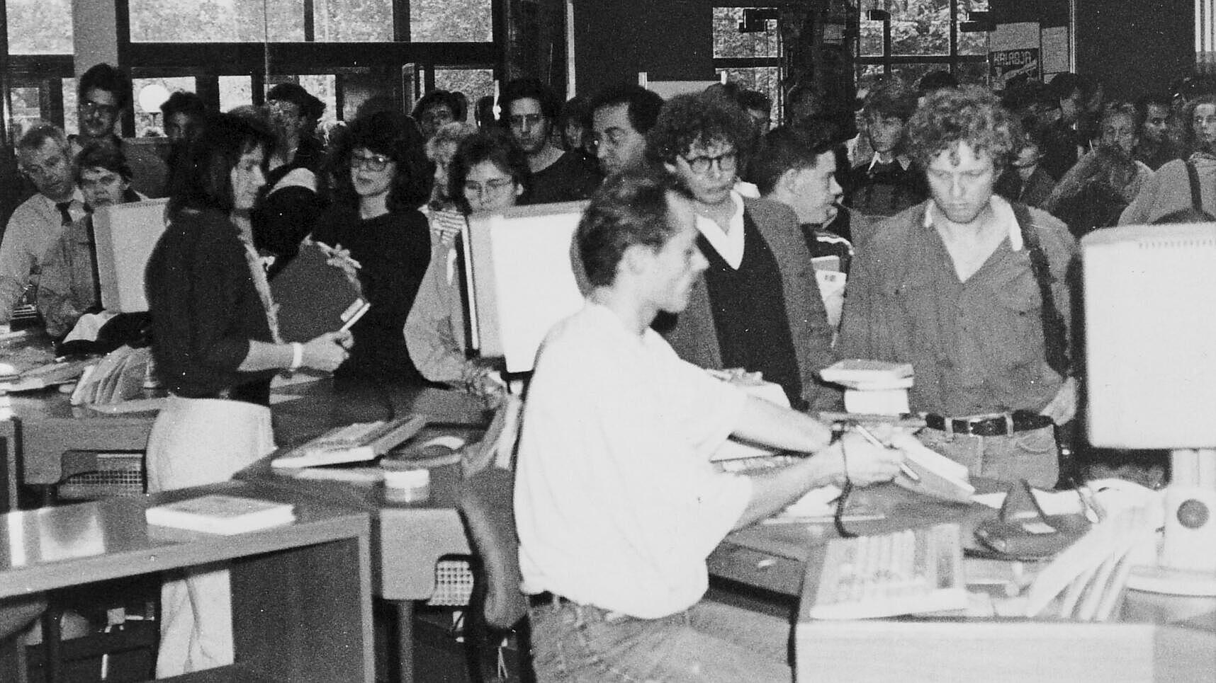 Black and white shot of many people with books in lending area of library