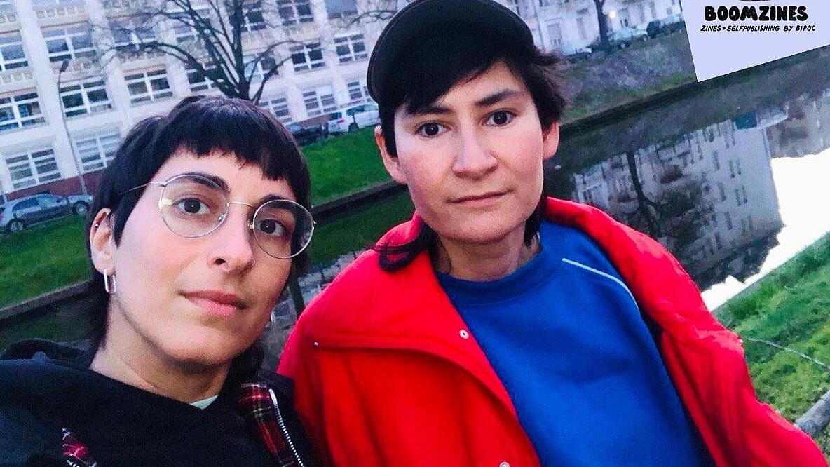 Selfie von zwei Personen, im Hintergrund ein Fluss und eine Häuserfassade