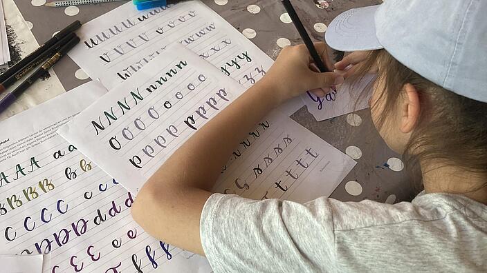 Ein Kind ist von hinten zu sehen, während sie kunstvoll Buchstaben malt