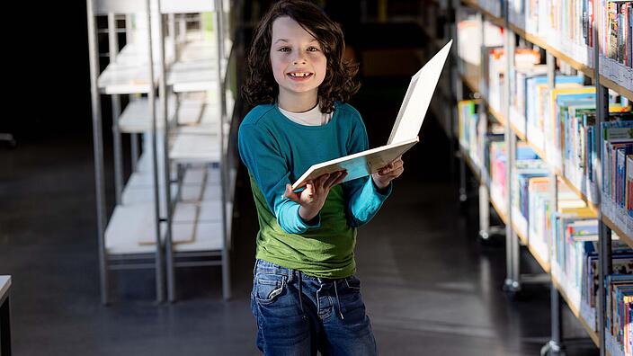 Junge mit Buch in der Hand lächelt in die Kamera