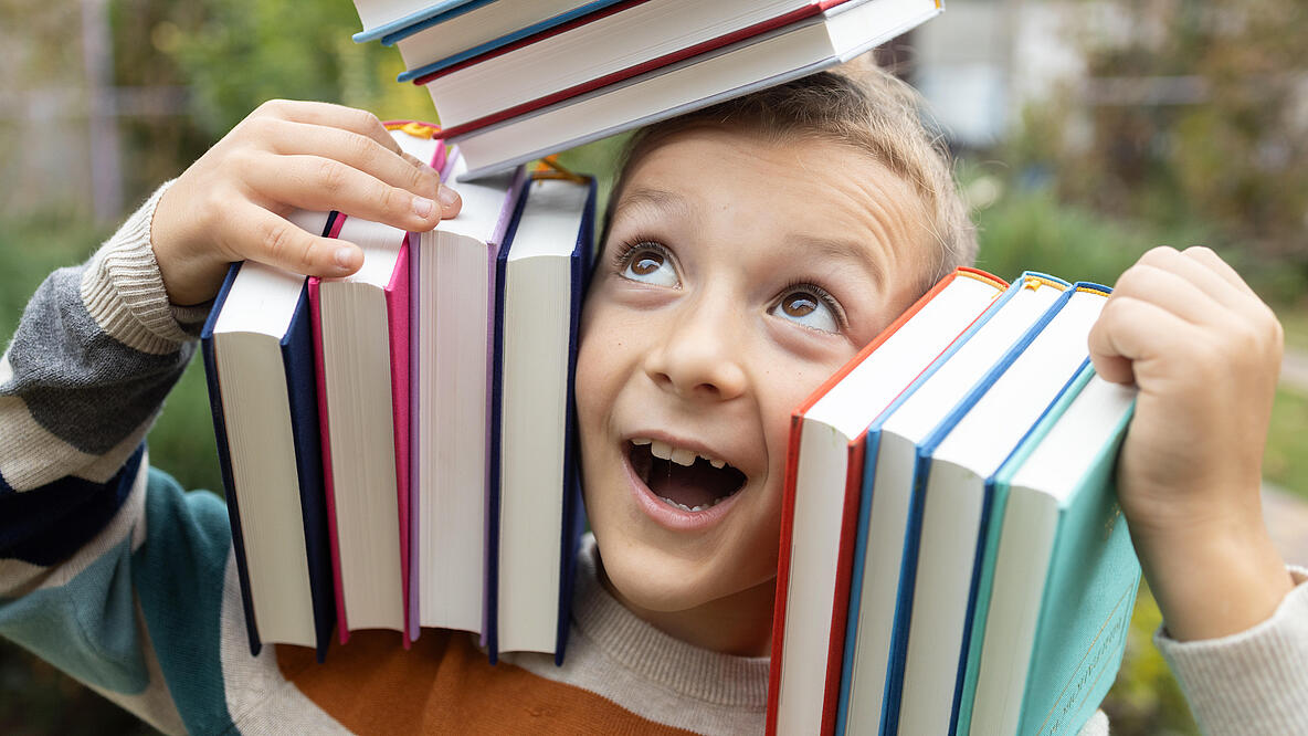 Junge balanciert Bücher auf dem Kopf und der Schulter links und rechts