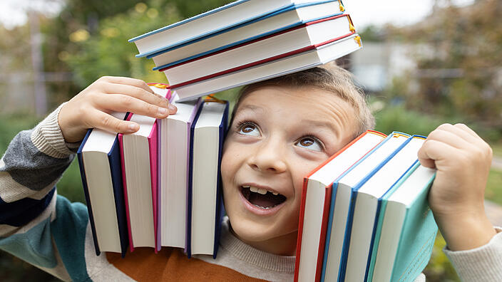Junge balanciert Bücher auf dem Kopf und der Schulter links und rechts