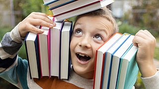 Junge balanciert Bücher auf dem Kopf und der Schulter links und rechts