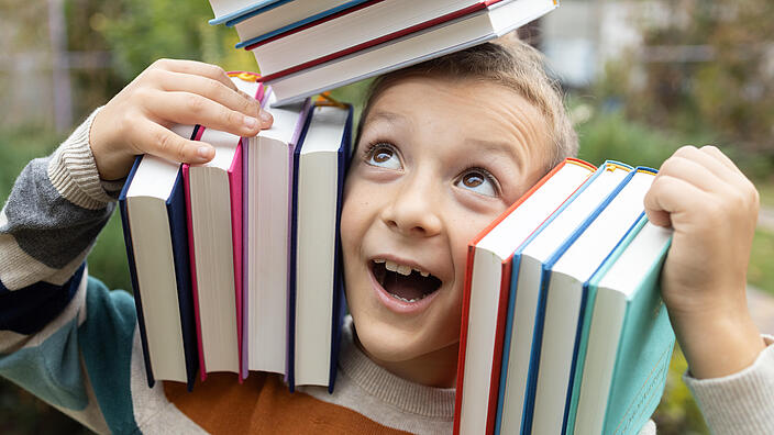 Junge balanciert Bücher auf dem Kopf und der Schulter links und rechts